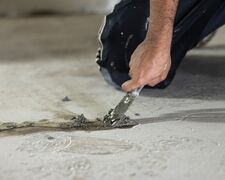 Handwerker kniet auf den Kellerboden und spachtelt einen undichten Riss zu