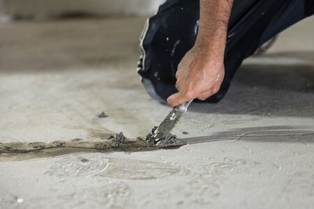 Handwerker kniet auf den Kellerboden und spachtelt einen undichten Riss zu